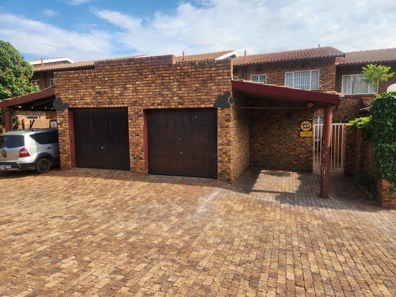 Front exterior view of a facebrick townhouse featuring a double garage, an attached carport, and paved driveway area.