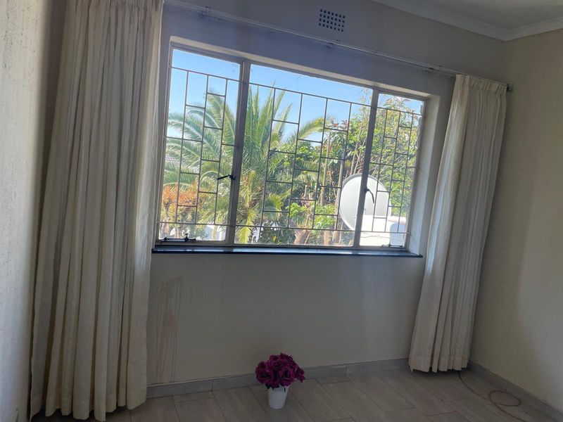 A bright, empty bedroom featuring tiled flooring, a large window with metal security bars, and neutral wall finishes.