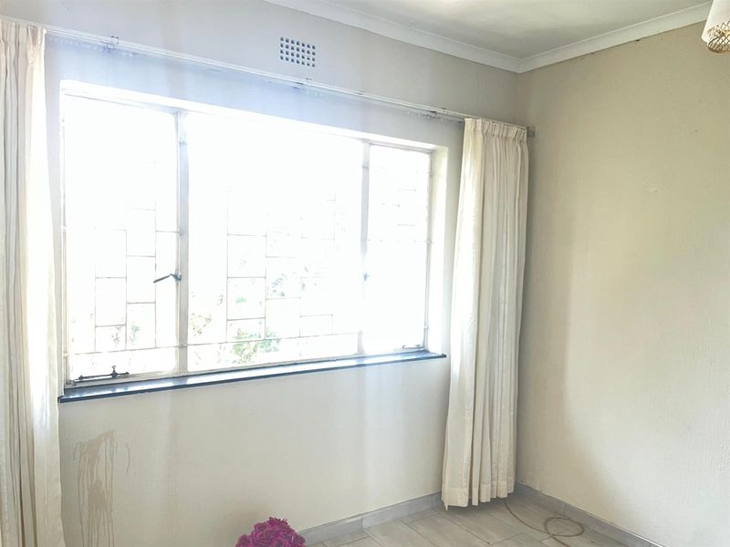 A bright, empty bedroom featuring tiled flooring, large windows with security bars, and neutral wall finishes, ready for a modern update.