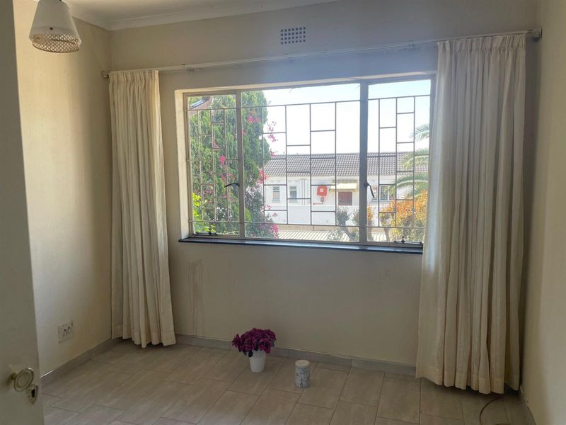 A vacant bedroom featuring tiled flooring, security bars on the window, and neutral wall finishes, offering a blank canvas for personalization.
