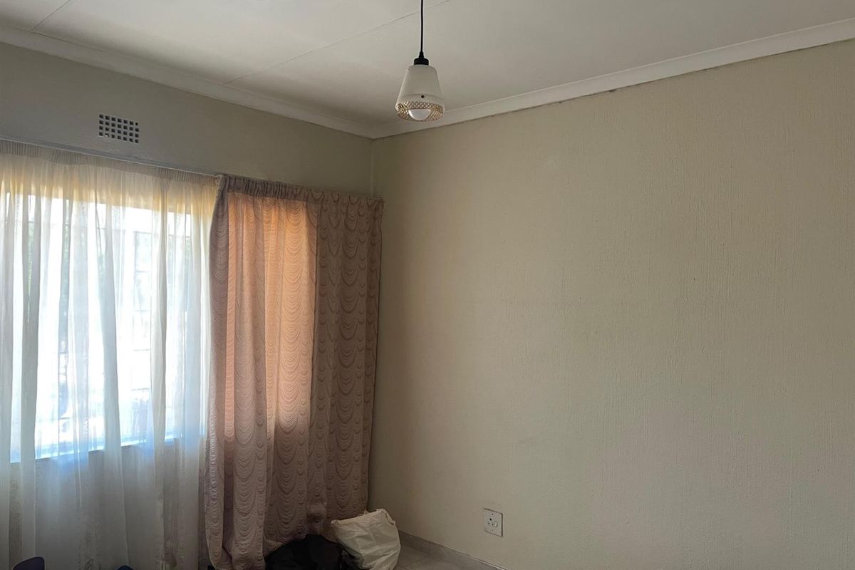A simple, empty bedroom featuring tiled flooring, neutral walls, and a central pendant light fixture, offering a blank canvas for personalization.