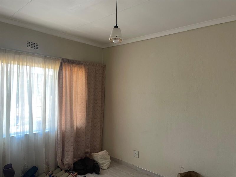 A simple, empty bedroom featuring tiled flooring, neutral walls, and a central pendant light fixture, offering a blank canvas for personalization.