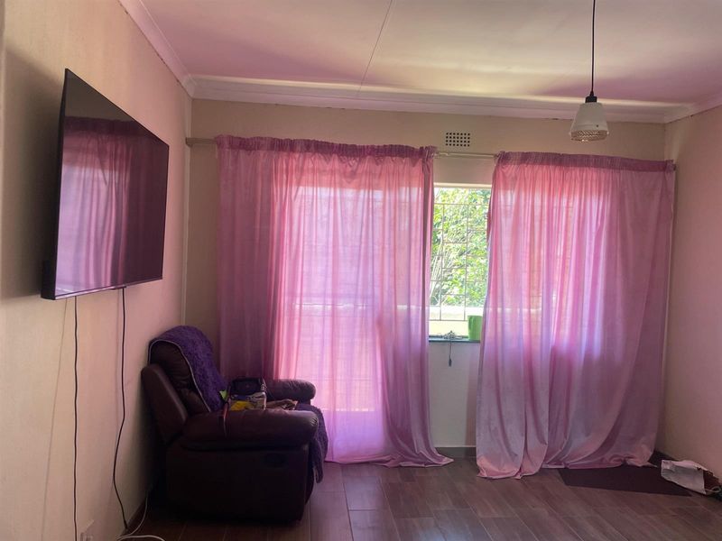 A living room featuring tiled flooring, a pendant light fixture, and a window fitted with security bars.