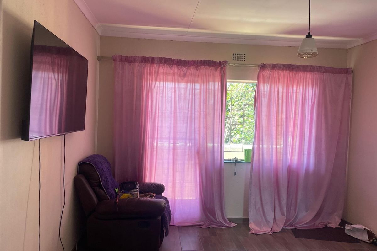 A living room featuring tiled flooring, a pendant light fixture, and a window fitted with security bars.