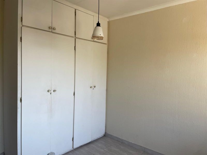 A simple bedroom featuring built-in cupboards with overhead storage, tiled flooring, and a neutral wall finish.