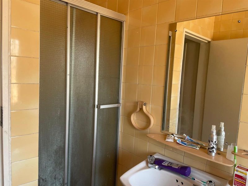 A dated bathroom featuring yellow wall tiles, a shower enclosure, and a wall-mounted mirror with a vanity shelf.