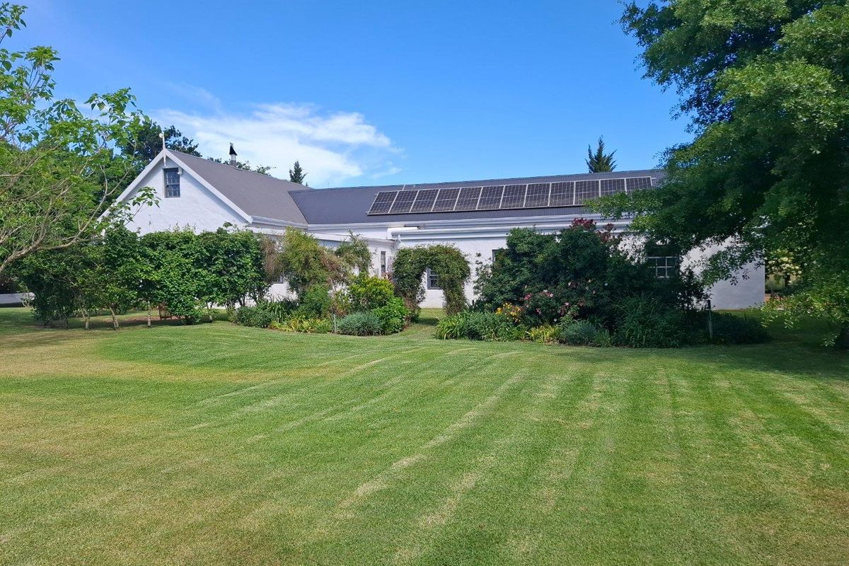 A well-maintained farm residence featuring a white exterior, a pitched roof, and a large array of roof-mounted solar panels set within a lush garden.