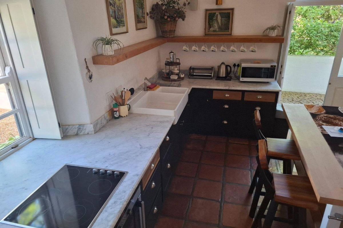 A charming farmhouse kitchen featuring dark cabinetry, marble countertops, a classic farmhouse sink, and terracotta floor tiles with direct access to the garden.
