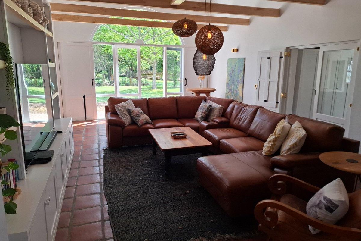 Spacious living room featuring exposed timber ceiling beams, terracotta tile flooring, and large arched glass doors providing views of the garden.