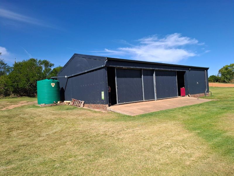 A functional farm outbuilding featuring dark corrugated metal cladding, sliding access doors, and an integrated water storage tank on a grassed lot.