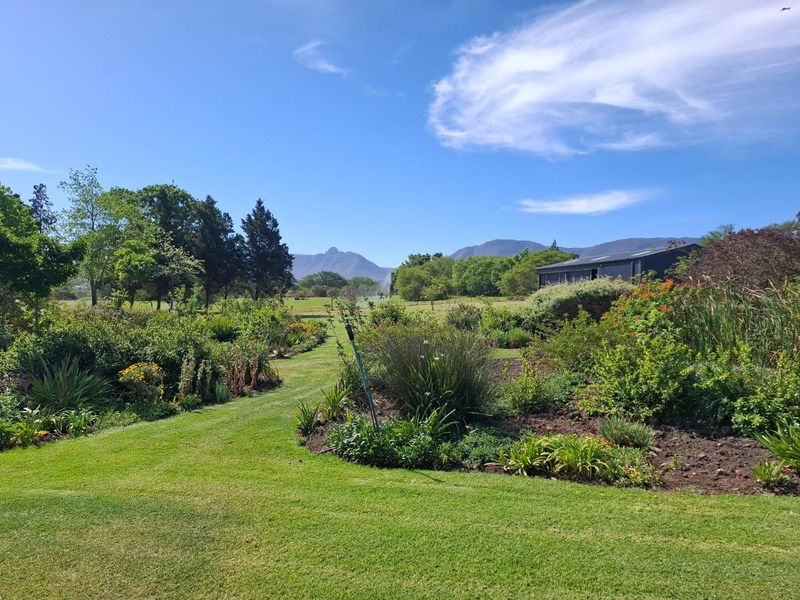 Expansive landscaped garden featuring lush green lawns, established shrubbery, and scenic mountain views on a farm property.