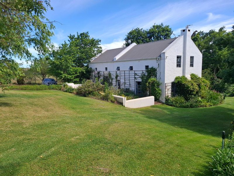 A charming white farmhouse exterior featuring a pitched roof, climbing plants on a trellis, and a well-maintained lawn in a peaceful rural setting.