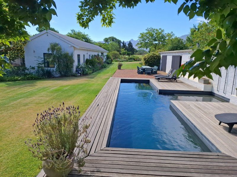 A well-maintained farm property featuring a rectangular swimming pool with timber decking, expansive lawn, and established garden views against a mountain backdrop.
