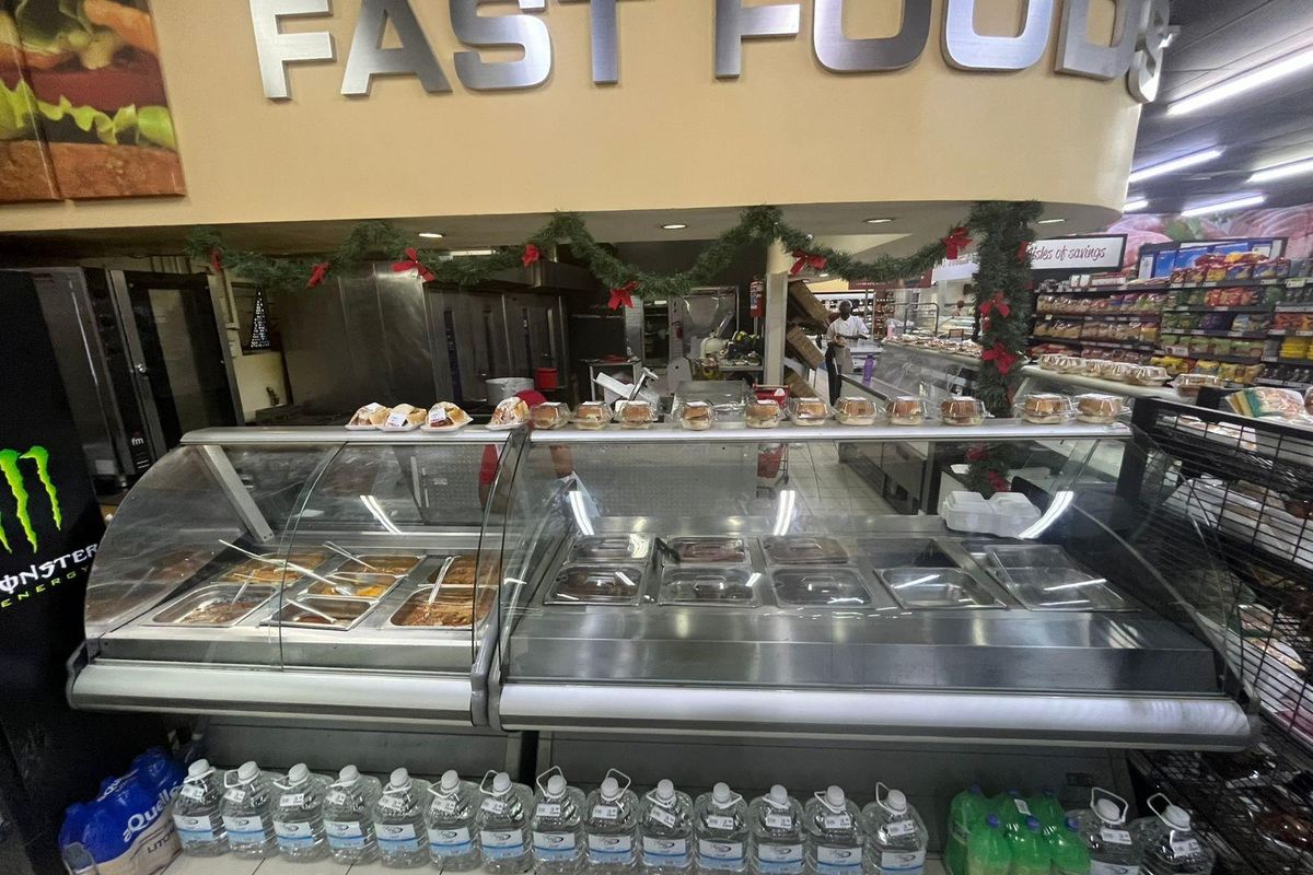 Commercial food service area featuring stainless steel refrigerated display counters, built-in food preparation stations, and overhead signage in a retail environment.