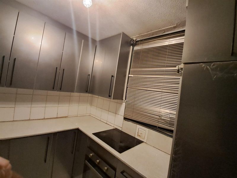 A compact kitchen featuring dark grey cabinetry, a built-in hob and oven, and a tiled backsplash, requiring some maintenance to the ceiling and finishes.
