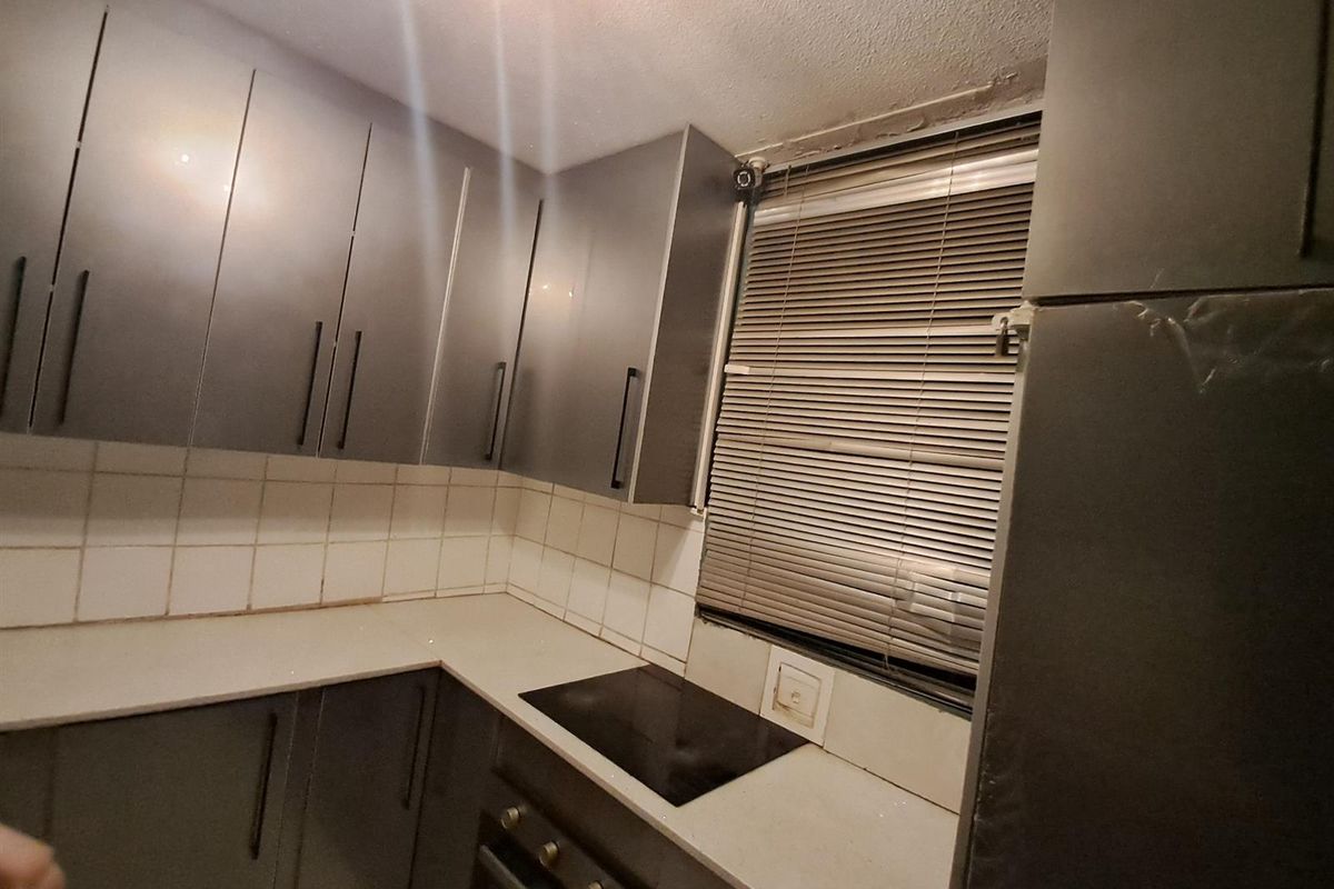 A compact kitchen featuring dark grey cabinetry, a built-in hob and oven, and a tiled backsplash, requiring some maintenance to the ceiling and finishes.