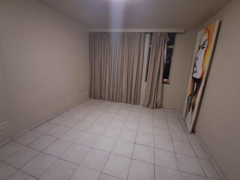 An empty bedroom featuring tiled flooring and large window curtains, presenting a blank canvas ready for personalization and minor cosmetic updates.