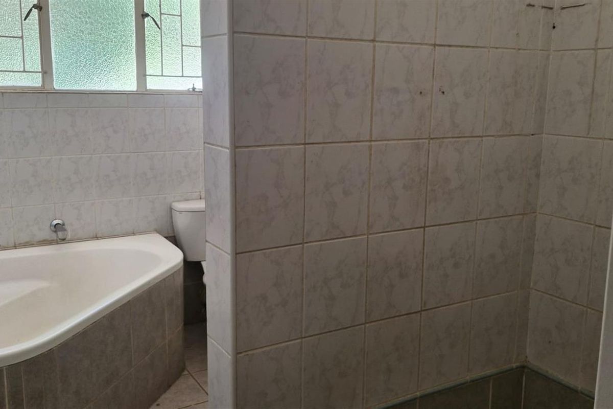 A dated bathroom featuring a built-in bathtub, tiled walls, and a separate shower area. The space requires modernization and new fixtures.