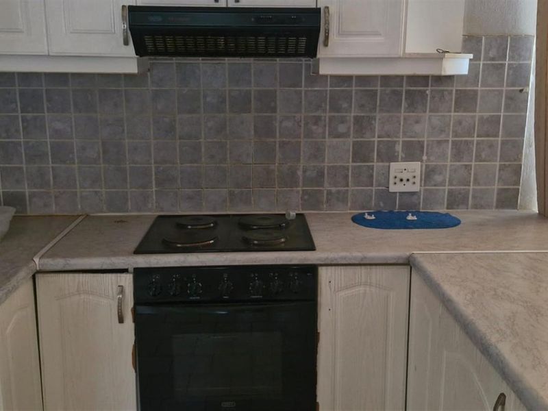 A functional kitchen featuring white cabinetry, laminate countertops, a tiled backsplash, and integrated cooking appliances including an electric hob and oven.