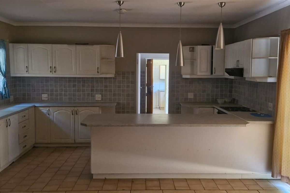 A functional kitchen featuring white built-in cabinetry, tiled backsplash, a breakfast bar, and integrated hob with extractor fan.