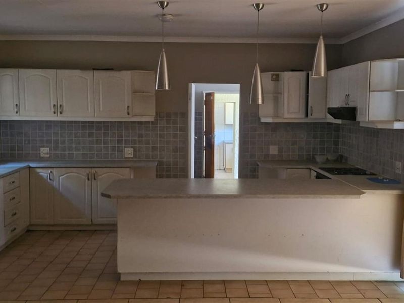 A functional kitchen featuring white built-in cabinetry, tiled backsplash, a breakfast bar, and integrated hob with extractor fan.