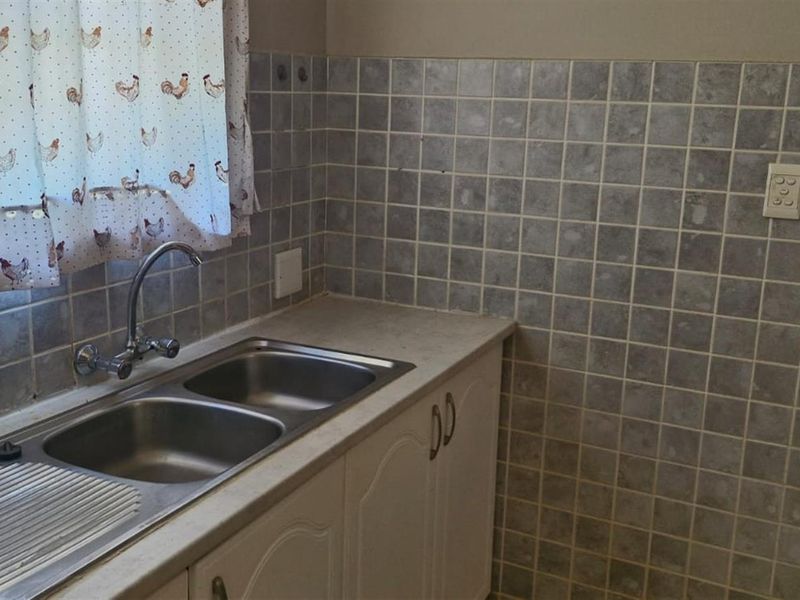A functional kitchen area featuring a double bowl stainless steel sink, laminate countertops, and tiled splashbacks, offering a dated but practical workspace.