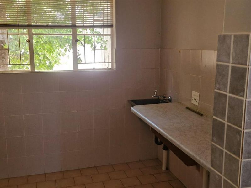 A functional laundry room featuring built-in cabinetry, a laminate countertop with a sink, and ceramic wall tiling.