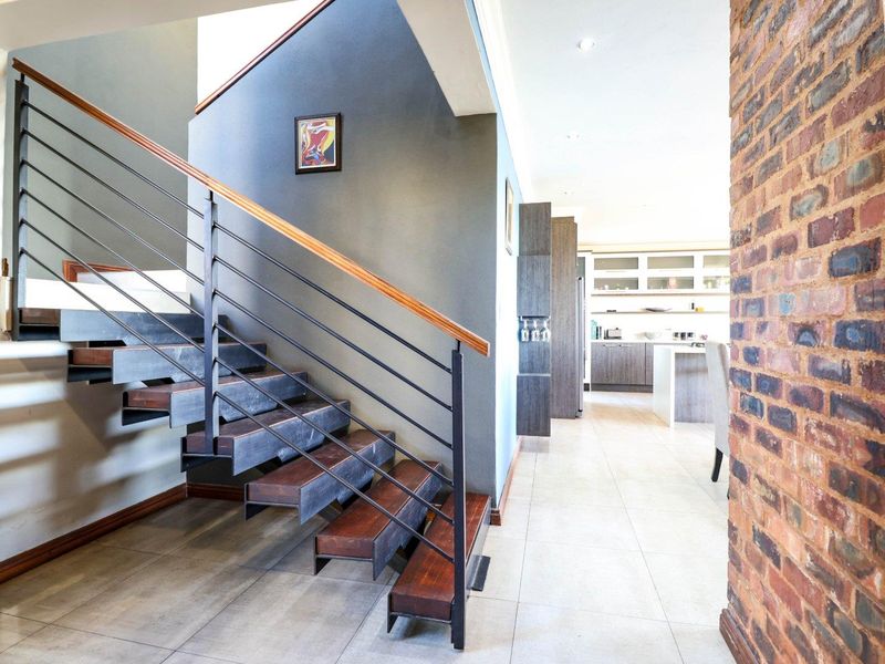 Modern open-plan living area featuring a striking floating staircase with metal railings, exposed brick accents, and sleek tiled flooring leading to the kitchen.
