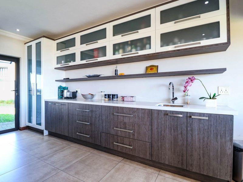 Modern scullery featuring dark wood-grain lower cabinetry, white stone countertops, an undermount sink, and ample glass-fronted upper storage with recessed lighting.