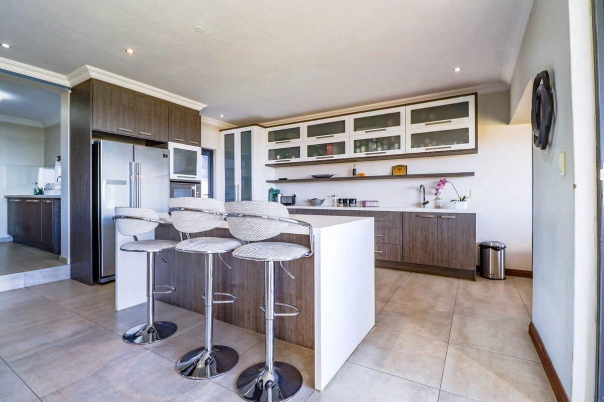Modern kitchen featuring a central island with breakfast bar seating, ample built-in cabinetry, stone countertops, and sleek tiled flooring.