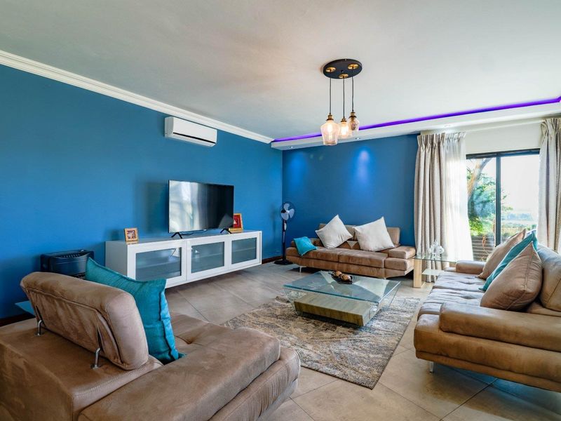 A well-maintained living room featuring tiled flooring, crown molding, recessed ceiling lighting, and a split-system air conditioner with access to an outdoor area.