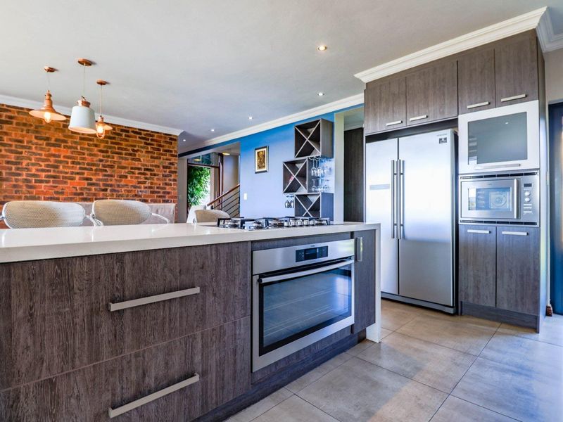 Modern open-plan kitchen featuring a central island with built-in oven and hob, sleek cabinetry, and an exposed brick feature wall.