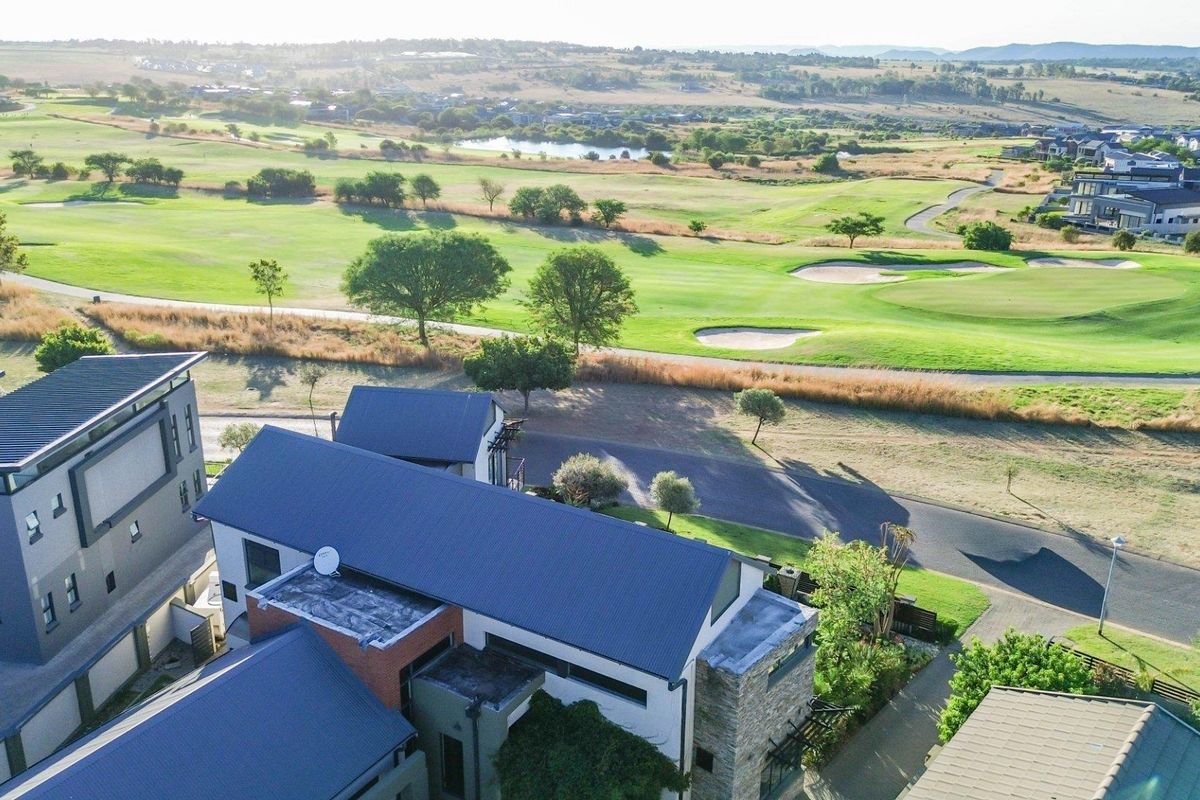 Aerial view of a modern residential property featuring a metal roof and stone cladding, situated overlooking a golf course estate.