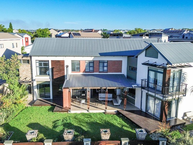 Aerial view of the rear elevation featuring a spacious covered patio, timber decking, landscaped garden, and a modern multi-story residential structure.