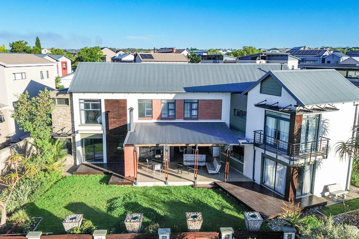 Aerial view of the rear elevation featuring a spacious covered patio, timber decking, landscaped garden, and a modern multi-story residential structure.