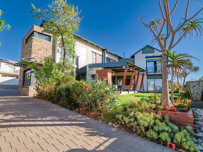 A modern multi-story residence featuring stone cladding, a paved driveway, a covered patio area, and well-maintained landscaped gardens.