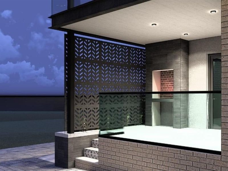 A modern covered patio featuring a built-in brick fireplace, decorative metal privacy screen, glass balustrade, and recessed ceiling lighting.