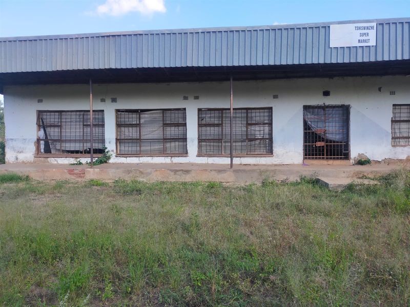 Front elevation of a commercial supermarket building featuring a corrugated metal roof, security-barred windows, and a concrete veranda.