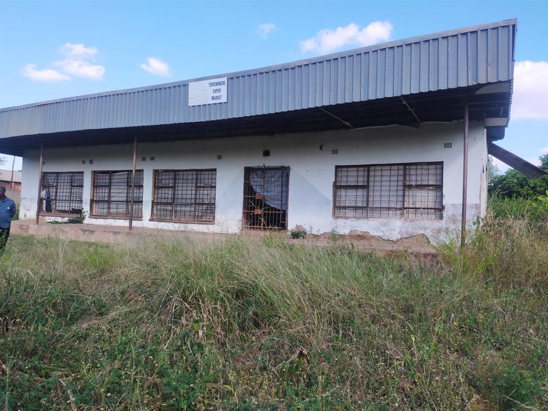 Front view of a commercial supermarket building featuring a corrugated metal roof, security bars on windows, and a security gate entrance.