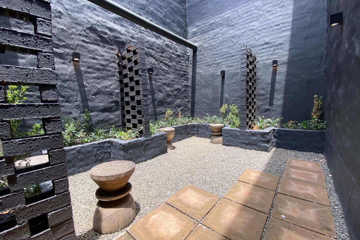 A private, enclosed rear courtyard featuring dark-painted brick walls, decorative brick privacy screens, raised garden beds, and a combination of gravel and paved surfaces.