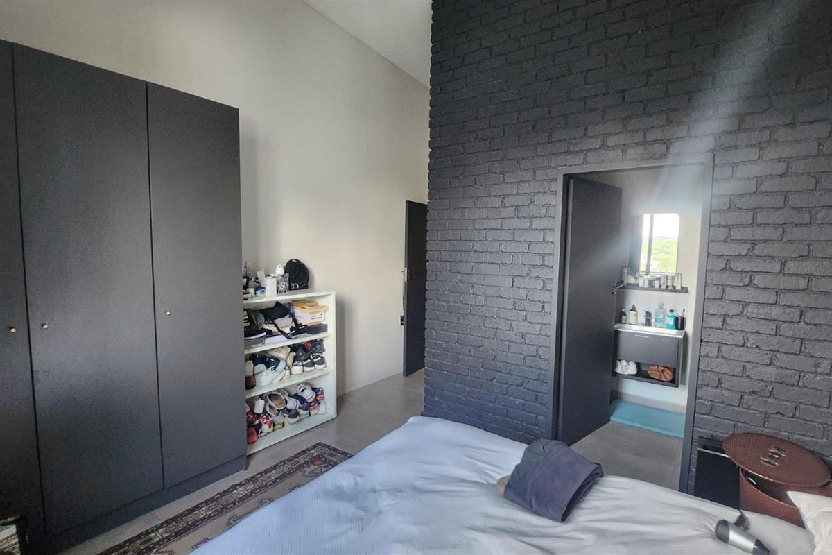 Bedroom featuring a dark exposed brick feature wall, built-in wardrobe, and direct access to an en-suite bathroom.