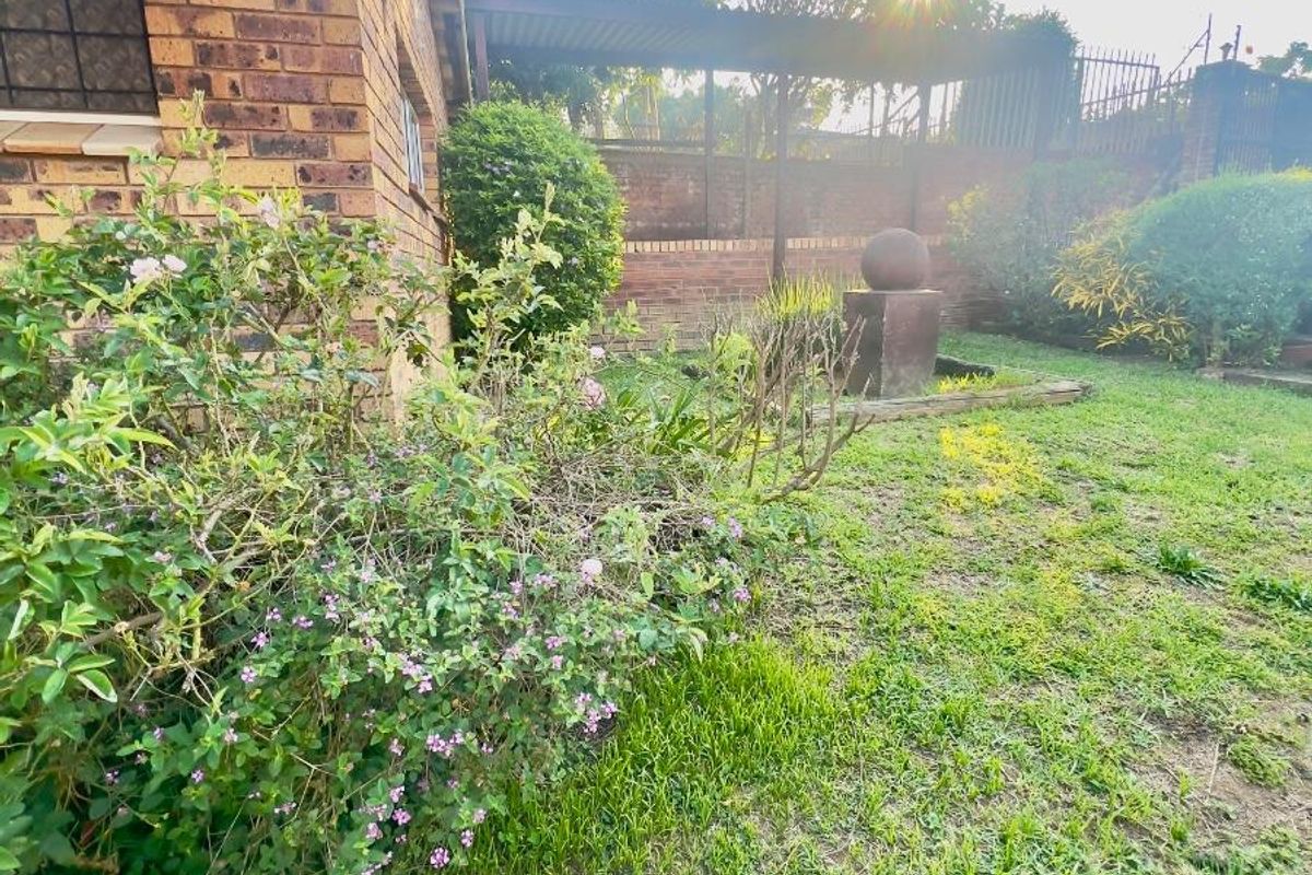 A view of the rear garden area featuring a brick exterior wall, established landscaping, and a decorative stone water feature.