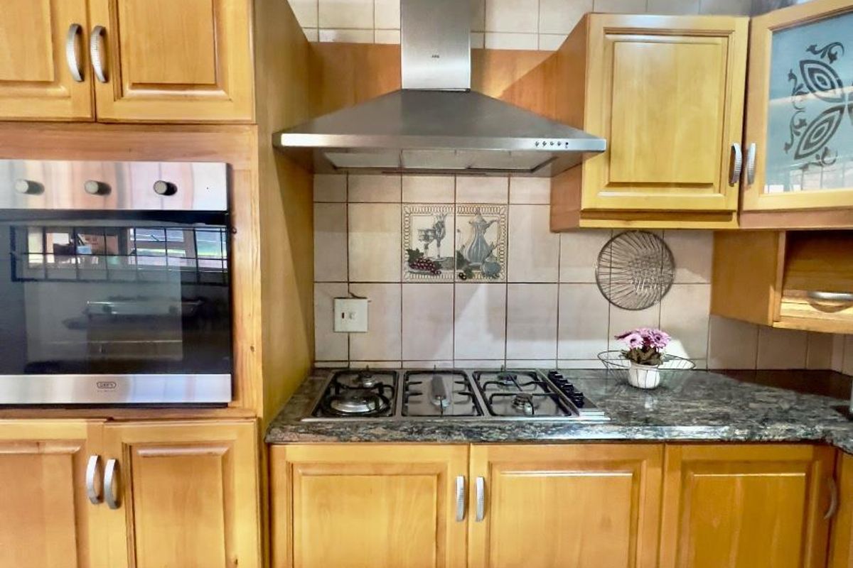 A functional kitchen featuring light wood cabinetry, granite countertops, a built-in oven, and a stainless steel extractor fan.