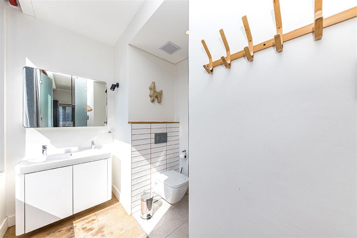 Modern bathroom featuring a wall-mounted toilet, vanity with integrated basin, mirrored cabinet, and tiled flooring.