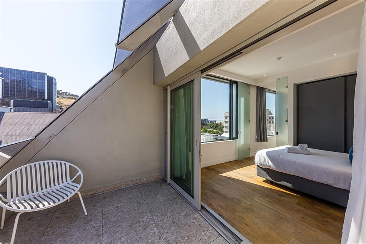 A modern bedroom featuring large sliding glass doors that open onto a private balcony with urban views and tiled flooring.