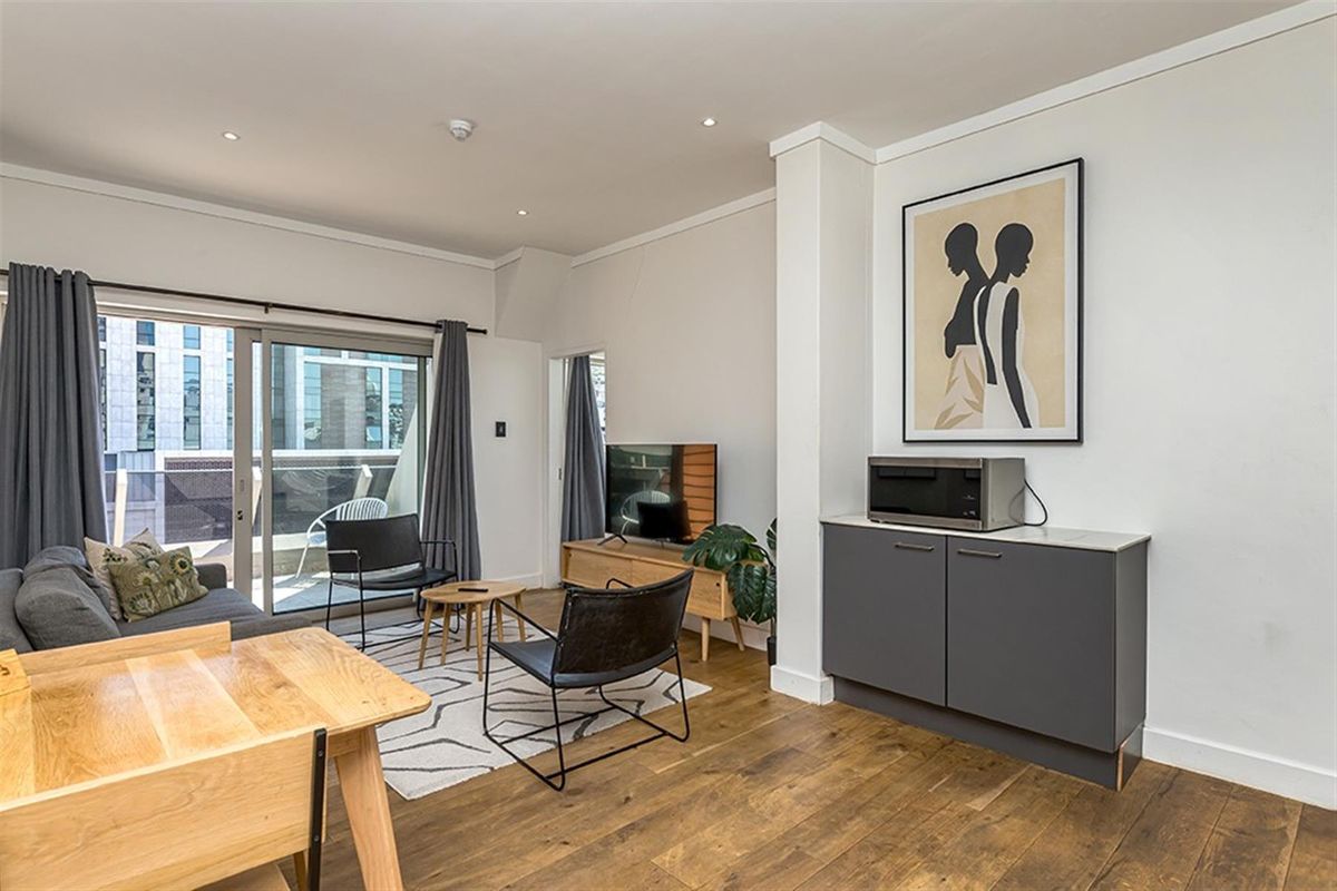 Open-plan living area featuring hardwood flooring, recessed lighting, and sliding glass doors leading to a private balcony.