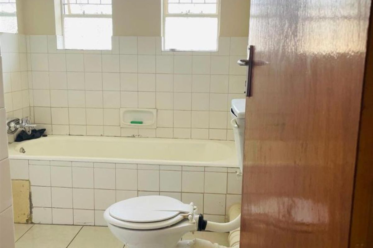 A dated bathroom featuring a bathtub, toilet, and tiled finishes. The space requires renovation to address exposed plumbing and worn fixtures.