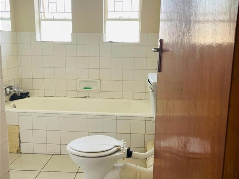 A dated bathroom featuring a bathtub, toilet, and tiled finishes. The space requires renovation to address exposed plumbing and worn fixtures.