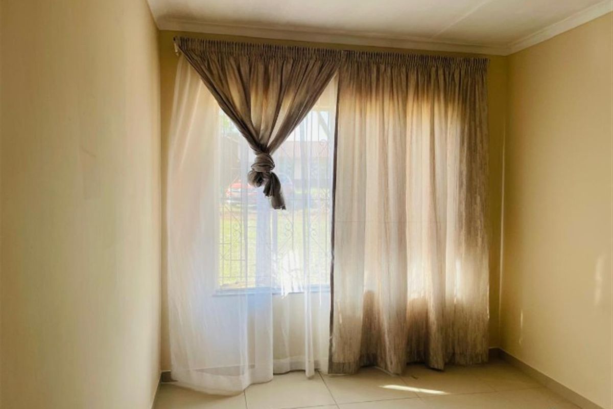 A vacant bedroom featuring tiled flooring and a window fitted with security bars, offering a blank canvas for interior design.