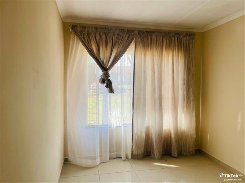 A vacant bedroom featuring tiled flooring and a window fitted with security bars, offering a blank canvas for interior design.